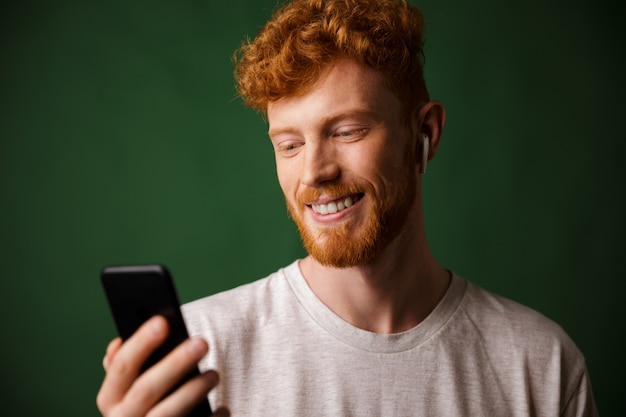 Primer plano de joven alegre pelirroja rizada barbudo joven, escuchando música con airpods