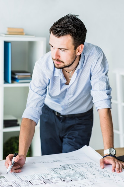 Primer plano de un joven arquitecto masculino con blueprint en el escritorio