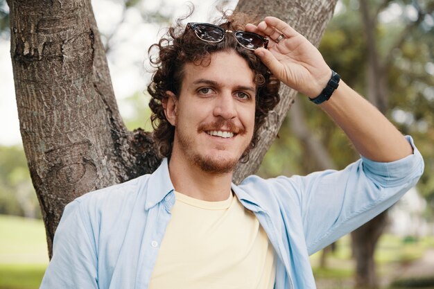 Primer plano de un joven caucásico posando para una foto al aire libre en el árbol