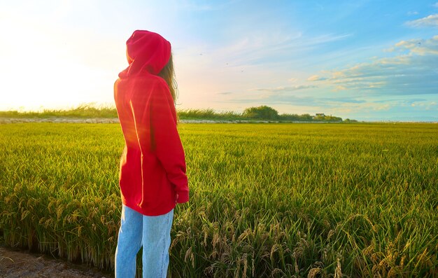 Primer plano de una joven dama en rojo alegremente de pie en un campo verde en un día soleado