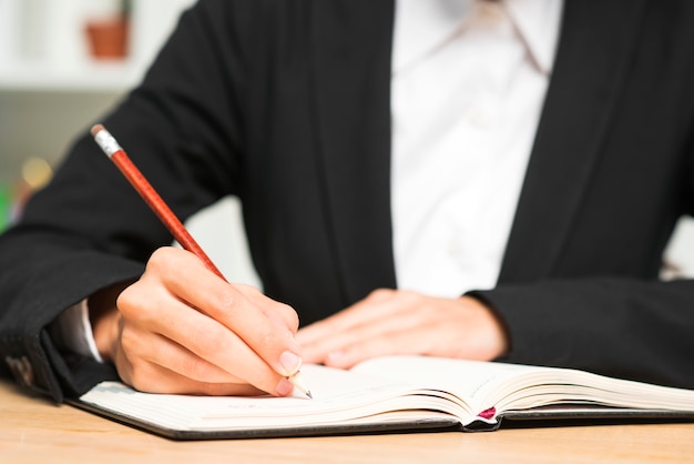 Primer plano de una joven empresaria escribiendo con lápiz rojo en el diario