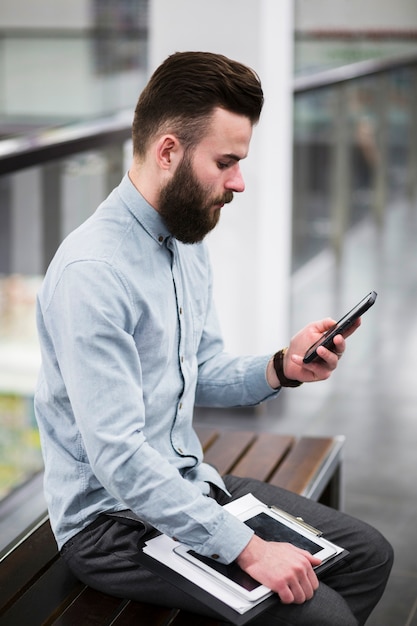 Primer plano de joven empresario sentado en el banco utilizando el teléfono móvil