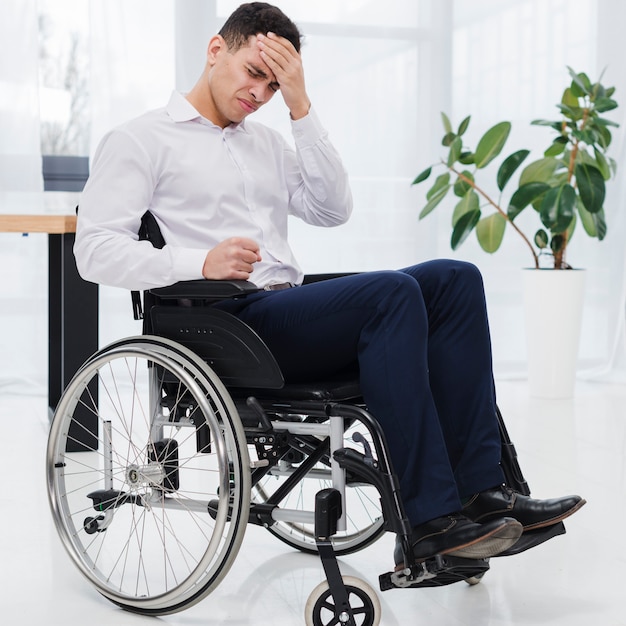 Primer plano de un joven empresario sentado en silla de ruedas que tiene dolor de cabeza