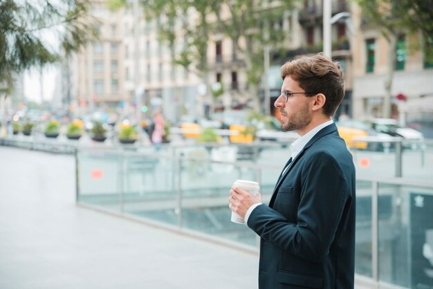 Primer plano de un joven empresario sosteniendo una taza de café disponible en la mano de pie en la calle