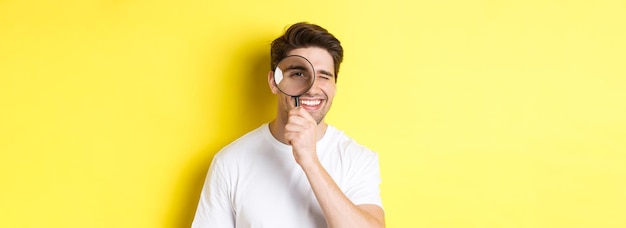 Foto gratuita primer plano de un joven mirando a través de una lupa y sonriendo buscando algo de pie