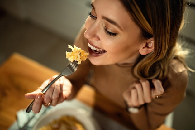 Primer plano de una joven mujer feliz comiendo pasta en la mesa de comedor