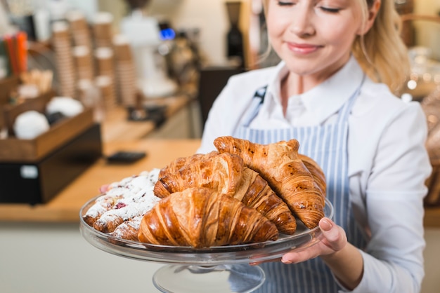 Primer plano de una joven sonriente que huele los croissants recién horneados en el soporte de la torta