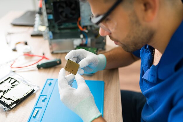 Primer plano de un joven técnico que usa gafas y guantes de protección mientras revisa el chip microprocesador dañado de una computadora