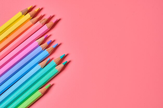 Primer plano de lápices de colores sobre una pared rosa con espacio de copia