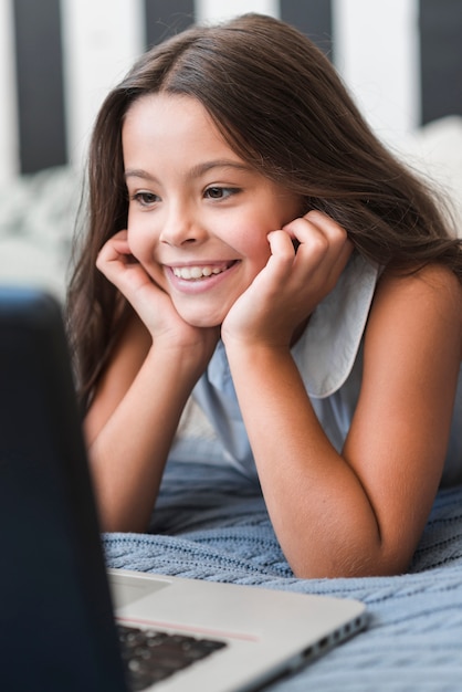 Primer plano de linda niña sonriente mirando portátil