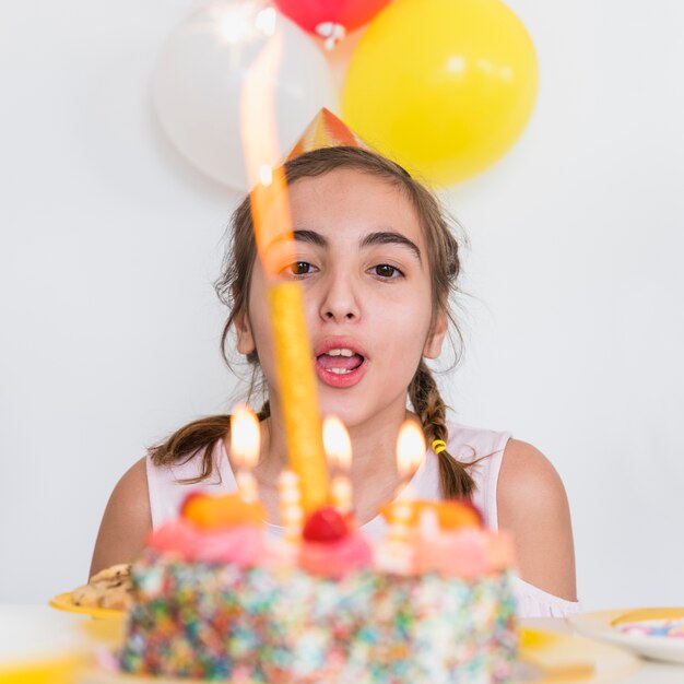 Primer plano de una linda niña soplando una vela en un delicioso pastel de cumpleaños en una fiesta