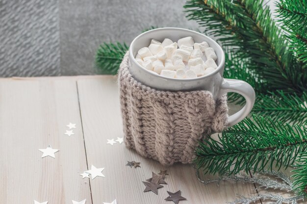 Primer plano de una linda taza llena de malvaviscos rodeada de adornos navideños en la mesa