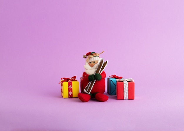 Primer plano de un lindo juguete de Santa Claus y coloridas cajas de regalo en el fondo púrpura