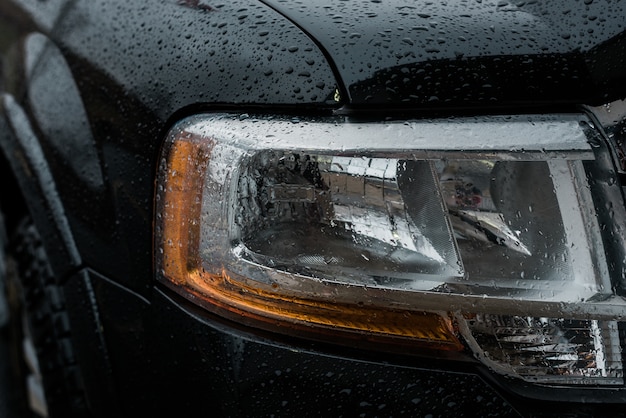 Primer plano de las luces delanteras de un coche cubierto por gotas de lluvia
