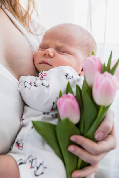 Primer plano de madre con bebé durmiendo y flores de tulipán rosa