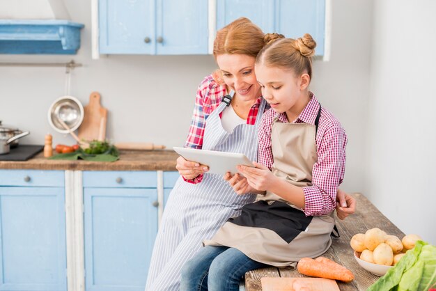 Primer plano de madre e hija mirando tableta digital en la cocina