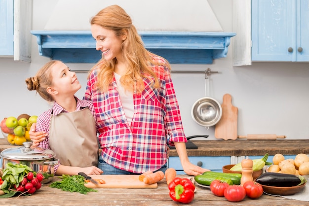 Primer plano de una madre y su hija mirando el uno al otro de pie frente a la mesa con verduras de colores