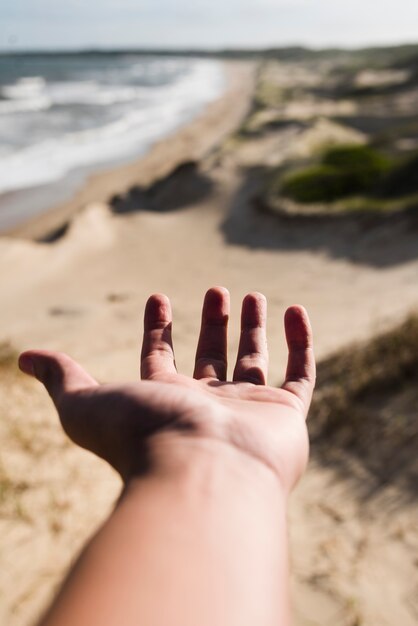 Primer plano mano alcanzando en el paisaje de la playa