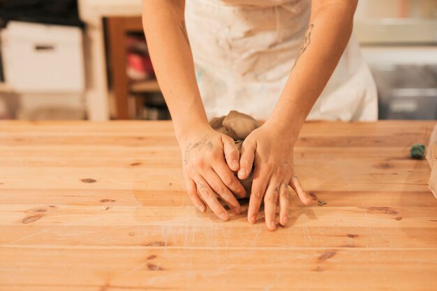 Primer plano de la mano del alfarero femenino amasando la arcilla en la mesa en el taller