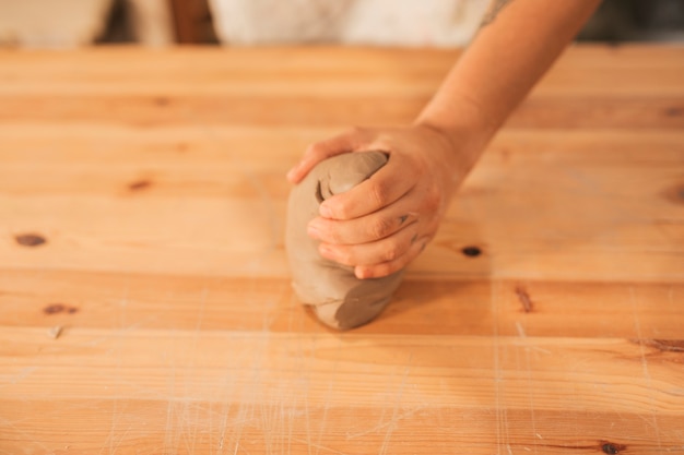 Primer plano de la mano del alfarero femenino amasando la arcilla en superficie de madera