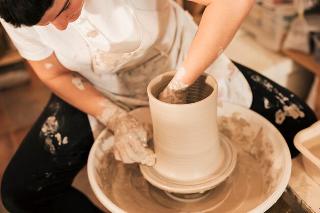 Primer plano de la mano del alfarero femenino haciendo una olla de barro en la rueda de alfarería