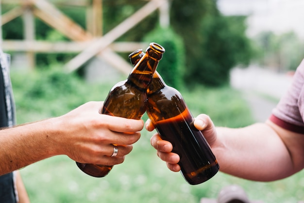 Primer plano de la mano de un amigo brindando botellas de cerveza marrón al aire libre