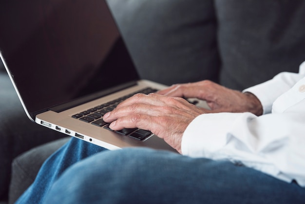 Primer plano de la mano de un anciano escribiendo en la computadora portátil