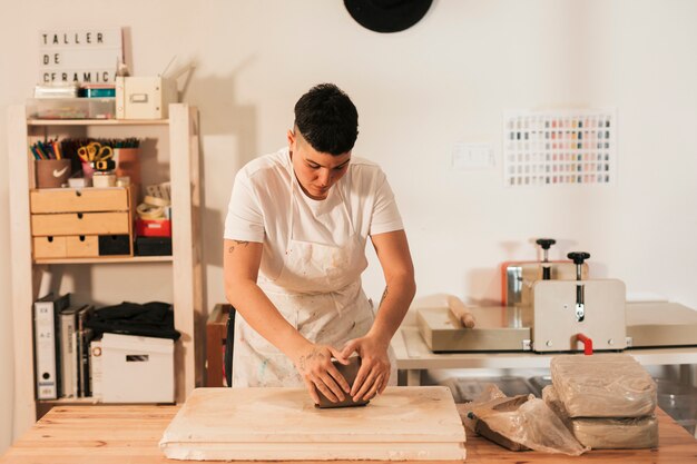 Primer plano de la mano de la artesana amasando una arcilla sobre tabla de madera en el taller