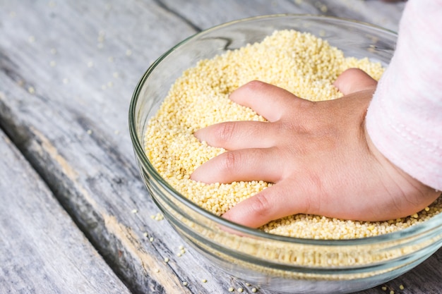 Primer plano de la mano de un bebé puesta en un tazón de grano de amarath entero fresco