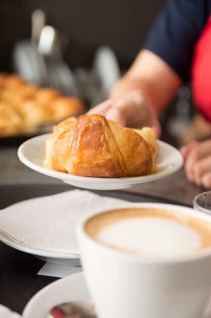 Primer plano de la mano de la camarera ofreciendo croissant al horno