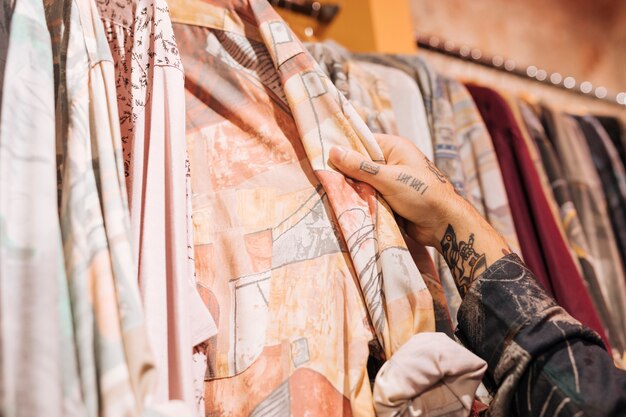 Primer plano de la mano del cliente masculino que elige la camisa que cuelga en el carril en la tienda