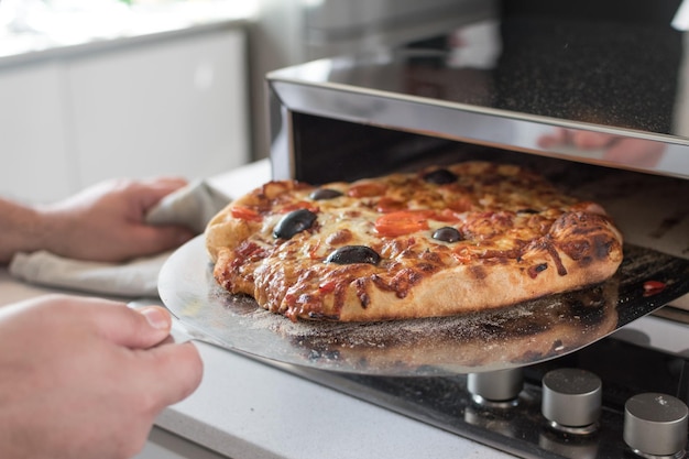 Primer plano de una mano de cocinero macho quitando pizza horneada del horno