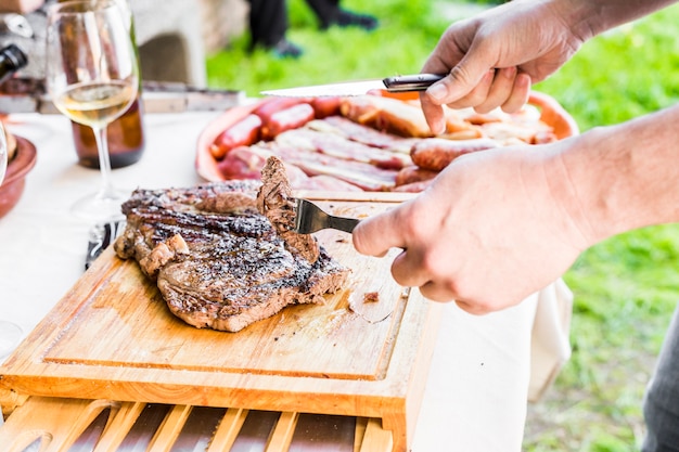 Primer plano de mano cortando carne fresca a la parrilla en la mesa al aire libre