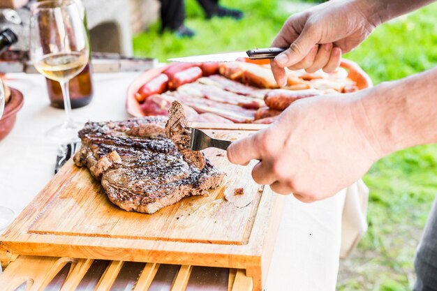 Primer plano de mano cortando carne fresca a la parrilla en la mesa al aire libre