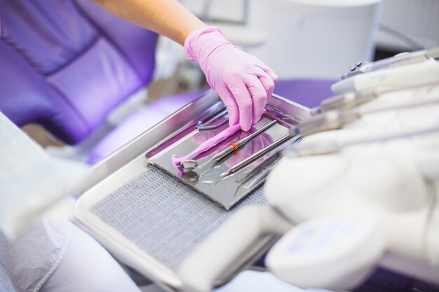 Primer plano de la mano de un dentista arreglando herramientas dentales en bandeja