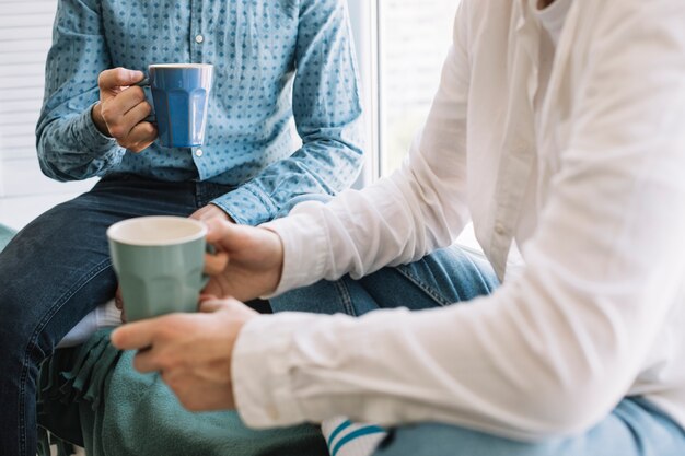 Primer plano de la mano de dos amigos sosteniendo la taza de café