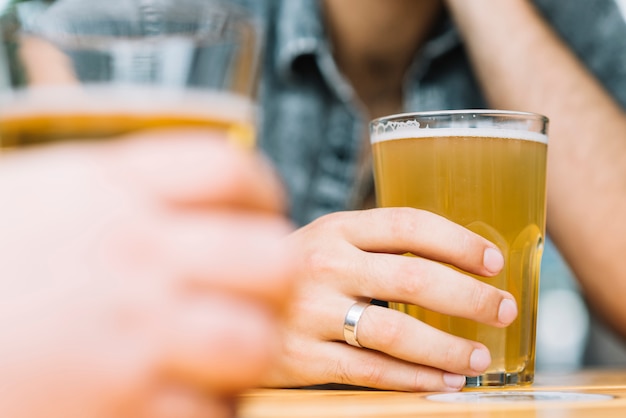 Primer plano de la mano de dos hombres con vaso de cerveza