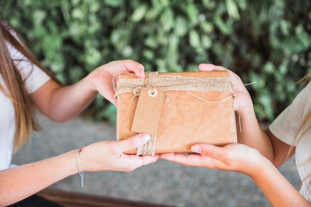 Primer plano de la mano de dos mujeres con caja de regalo marrón