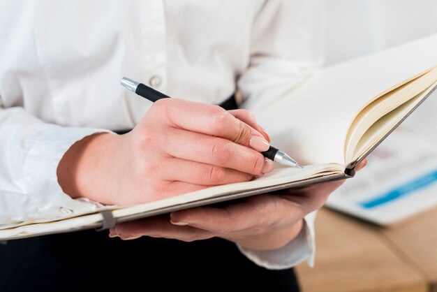 Primer plano de la mano de la empresaria escribiendo en el diario con la pluma