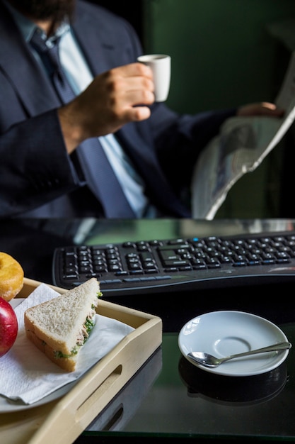 Foto gratuita primer plano de la mano de un empresario sosteniendo taza leyendo el periódico