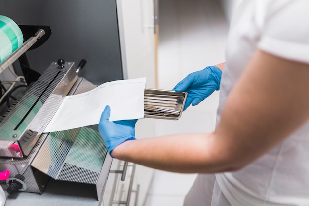 Primer plano de la mano de la enfermera que embala el instrumento dental con el plástico