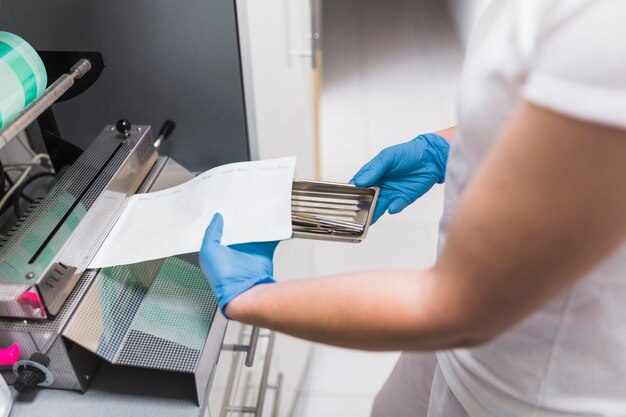 Primer plano de la mano de la enfermera que embala el instrumento dental con el plástico