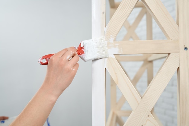 Primer plano de la mano femenina aplicando pintura blanca sobre un soporte de madera