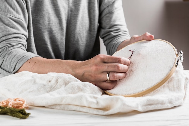 Primer plano de mano femenina bordado de costura en tela blanca