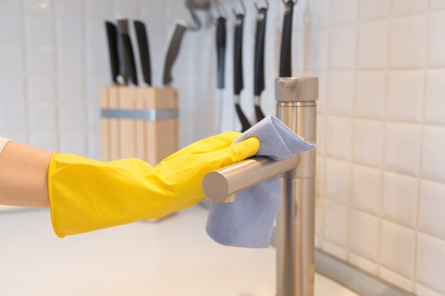 Primer plano de la mano femenina en guantes de limpieza de la cocina grifo