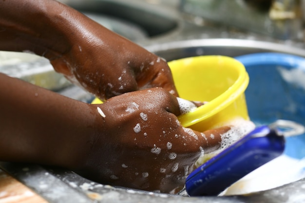 Primer plano de una mano femenina negra lavando un tazón amarillo