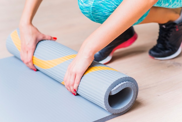 Primer plano de una mano femenina plegable estera de yoga