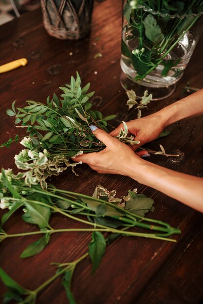 Primer plano de la mano de un florista que ordena las plantas en el escritorio de madera