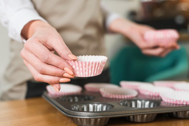 Primer plano de la mano de la hembra colocando vasos de papel en el molde para muffins