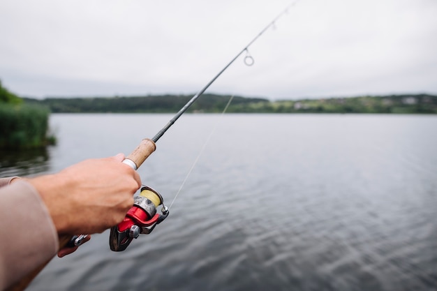 Primer plano de la mano del hombre con caña de pescar sobre el lago